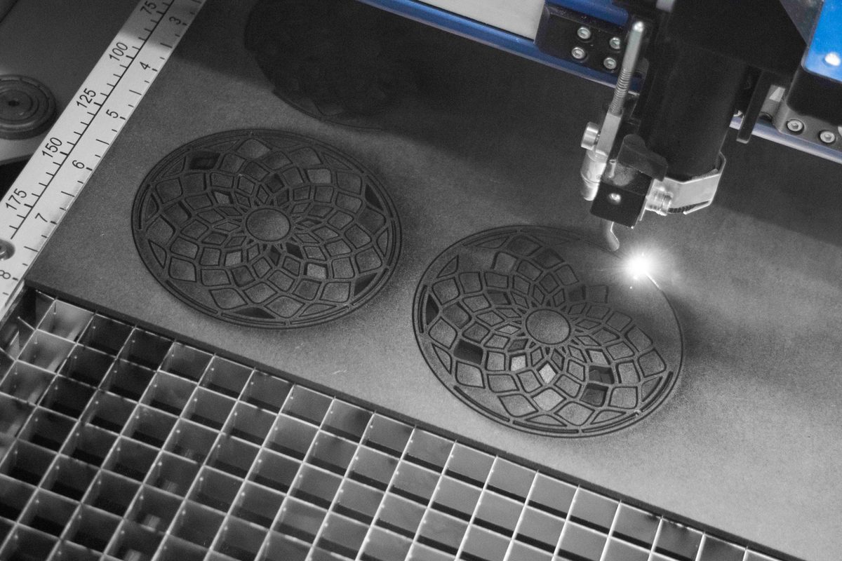 Close-up of a laser-engraved design in black-painted MDF — the laser removes the paint to reveal the pale MDF fibre beneath, producing crisp, high-contrast patterns